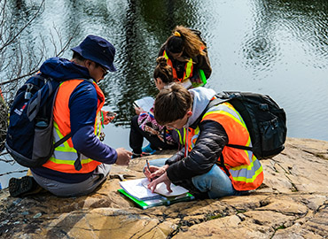 students taking notes on an outcrop next to water