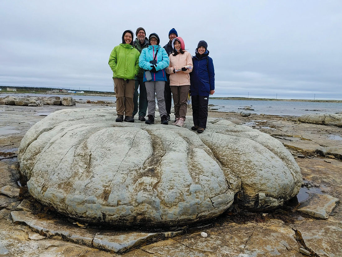 a group of student standing on a large rounded mound with the ocean in the background