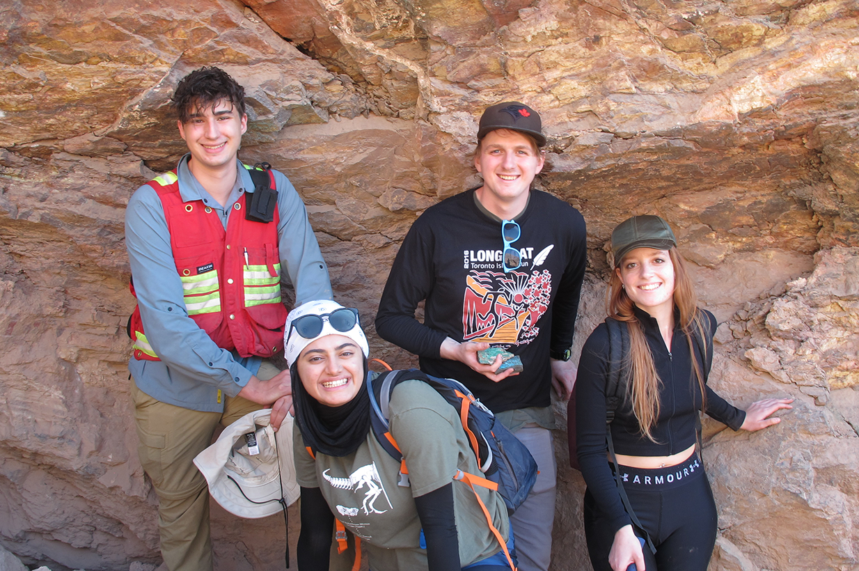 four people leaning against a reddish coloured rock