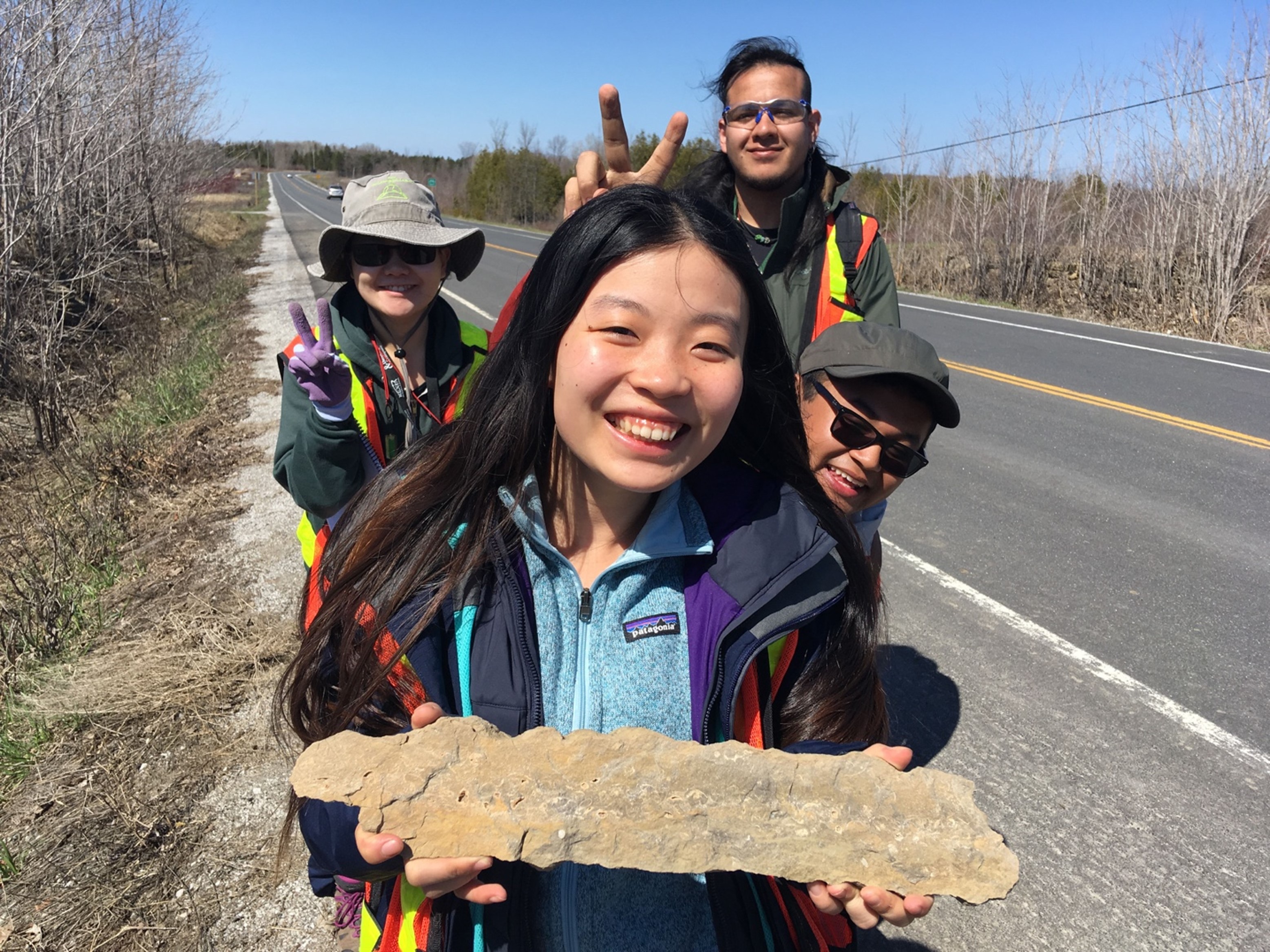 a smiling student holding a rock sample while friends do fun poses around them