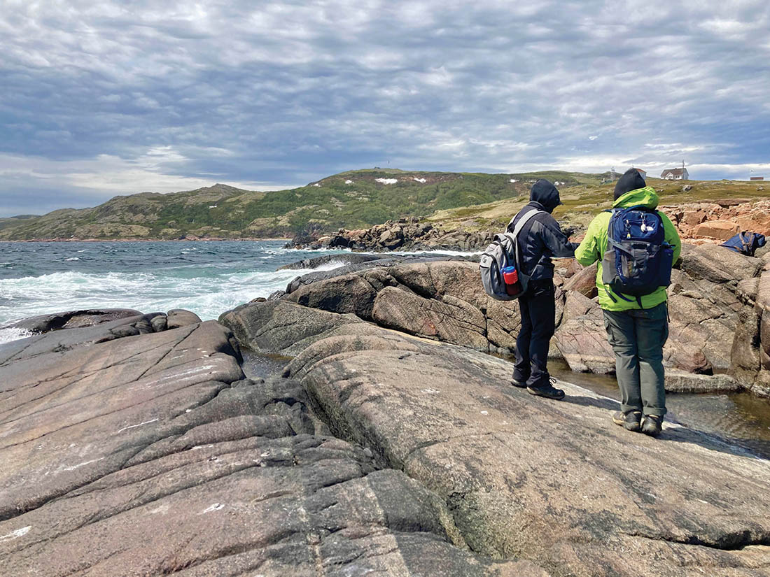 two students taking notes while standing on the rocks next to the ocean