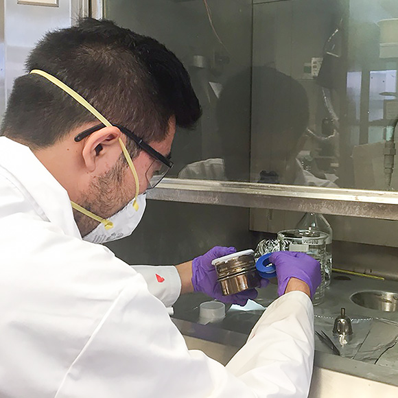 a scientist wearing a mask and gloves working at a fume hood