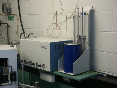 a n instrument with dials nesr the bottom next to a blue cylinder shaped object with tubing connected to it in a lab
