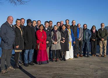 a group of 20 smiling people standing on a wooden walkway next to water