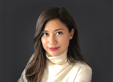 headshot of person with dark hair and white sweater looking at camera