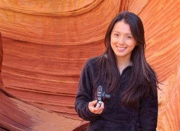Corliss Sio in front of orange red coloured rock holding a camera