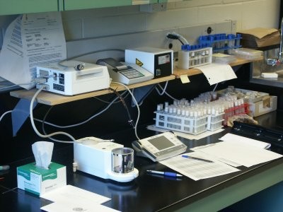 a lab counter top with digital weighing equipment, a variety of test tubes, papers and pens